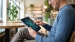 Un homme souriant utilise une tablette numérique affichant des icônes de réseau interconnectées dans un café.